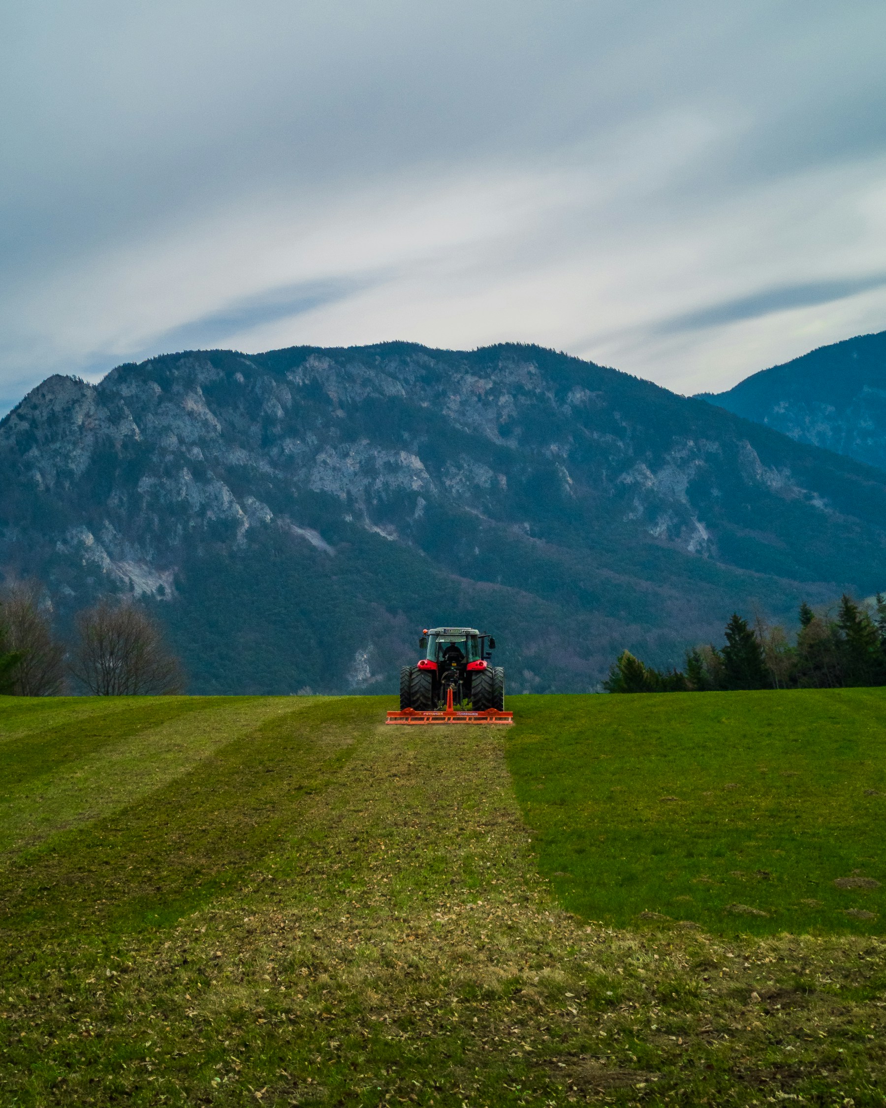 Traktor auf Grünland vor Wald und Bergen.